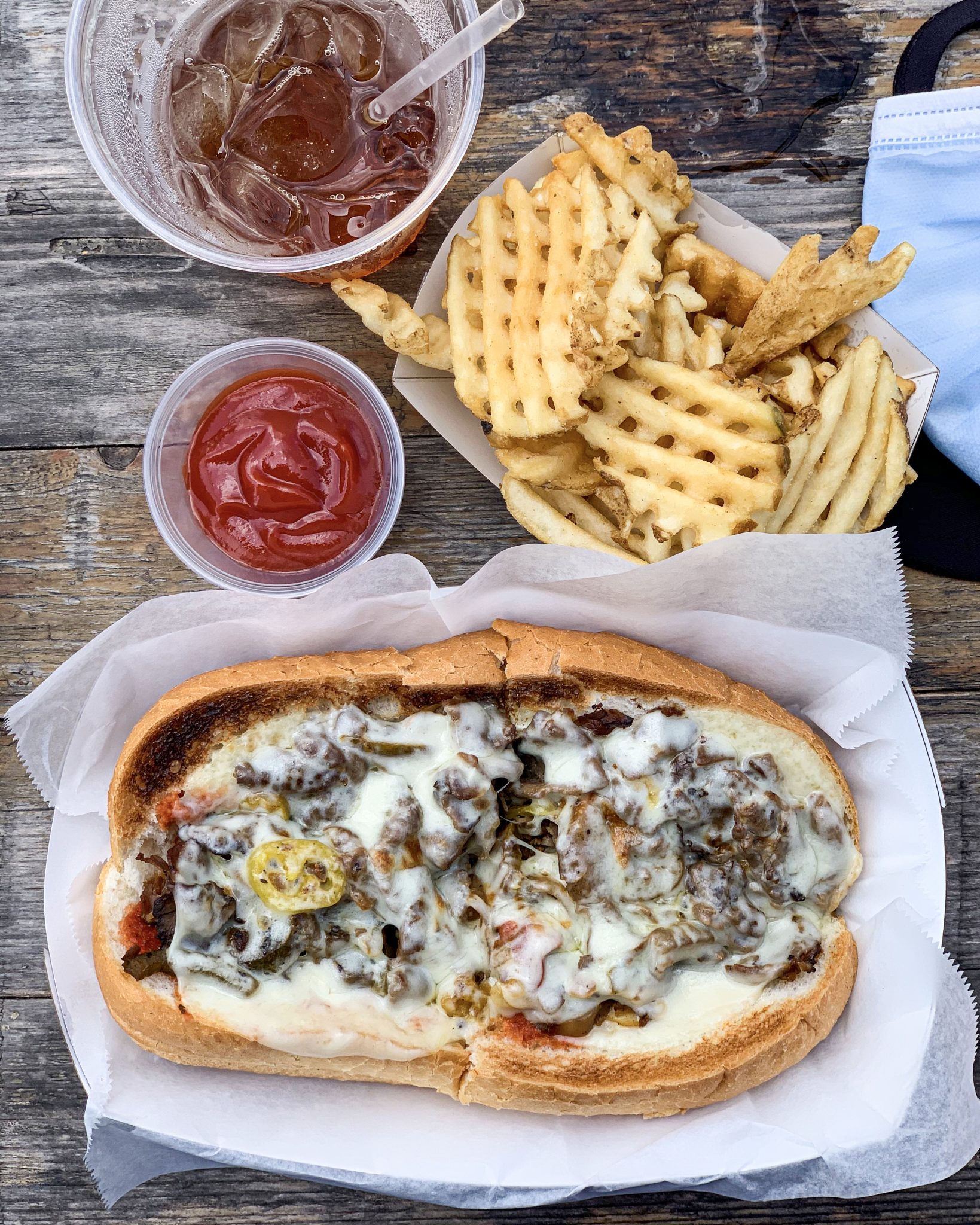 Top view of a Philly cheesesteak, fries, and ketchup on a wooden table