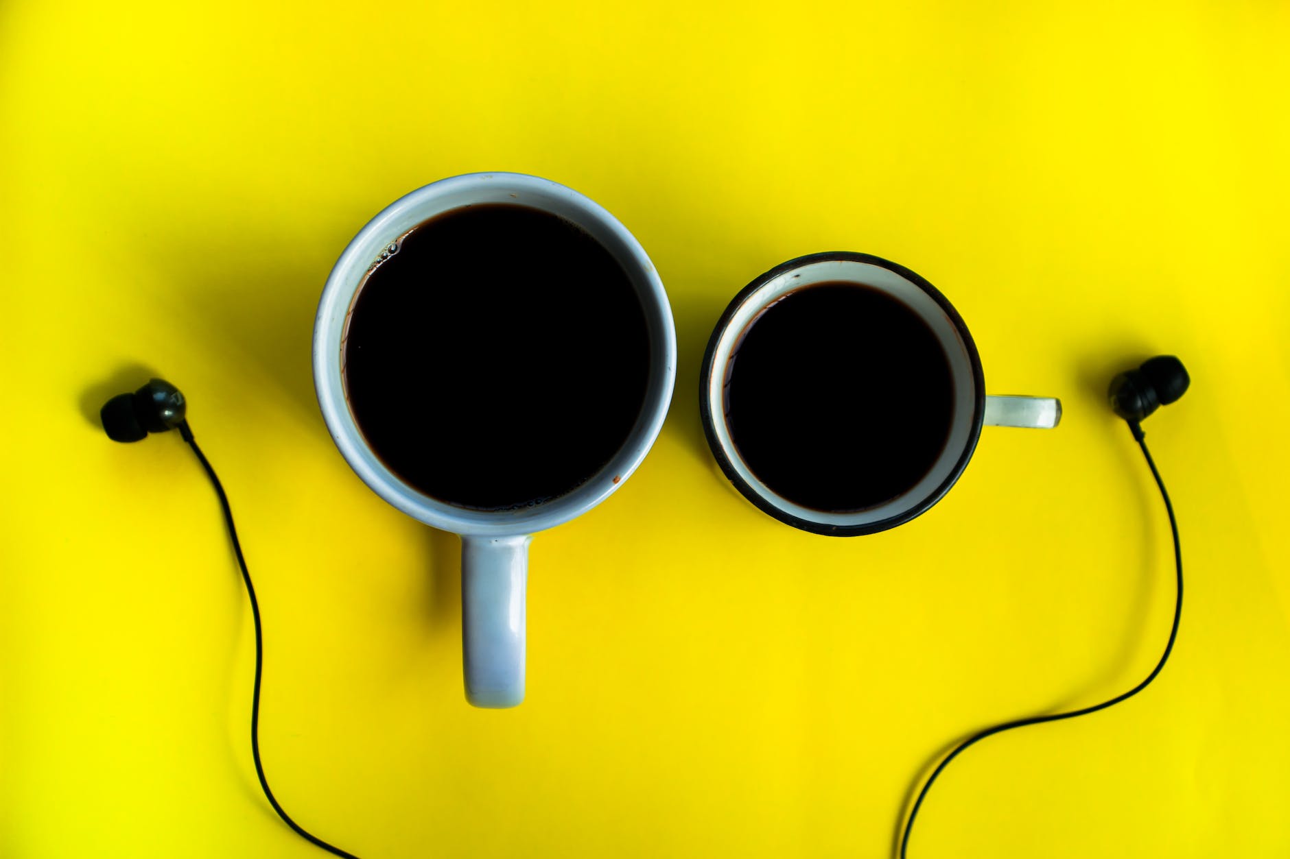 mugs with coffee near earphones on yellow background